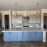 Modern Houston kitchen with refinished blue and white cabinets, sleek white countertops, mosaic backsplash, and pendant lights showcasing the Piper family's cabinet refinishing skills