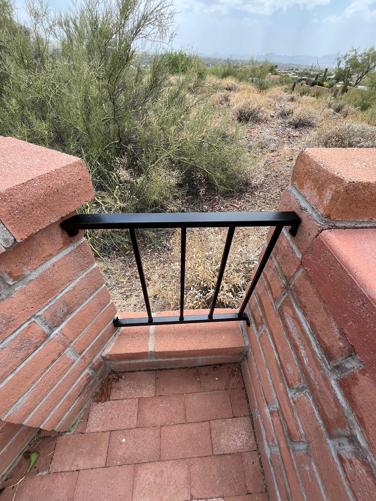 Gate and Fence Painting in Tucson featuring a sleek black wrought iron fence set in a red brick wall, blending with the desert landscape and enhancing outdoor aesthetics.