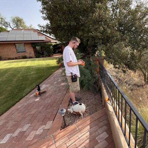 Gate and fence painting in Tucson with a person prepping a metal fence using painter’s tape in a suburban yard with tools neatly arranged nearby.