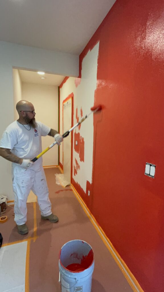 Interior painting in Tucson showing a painter applying bold red paint to a wall with a roller, creating a vibrant and warm atmosphere in a well-prepped room.