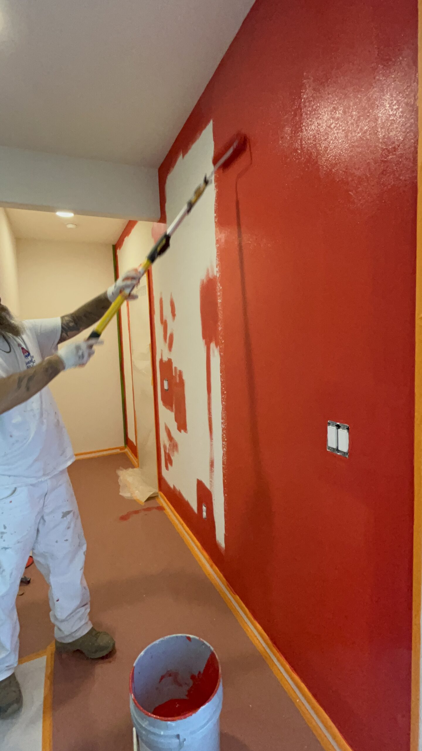 Interior painting in Tucson showing a person using a roller to apply vibrant red paint to a wall with precision, care, and professional technique.