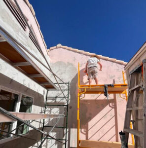 Piper Family Painting Company worker prepares building exterior under blue skies, showcasing Vail Painting Company’s expert surface prep and renovation process.